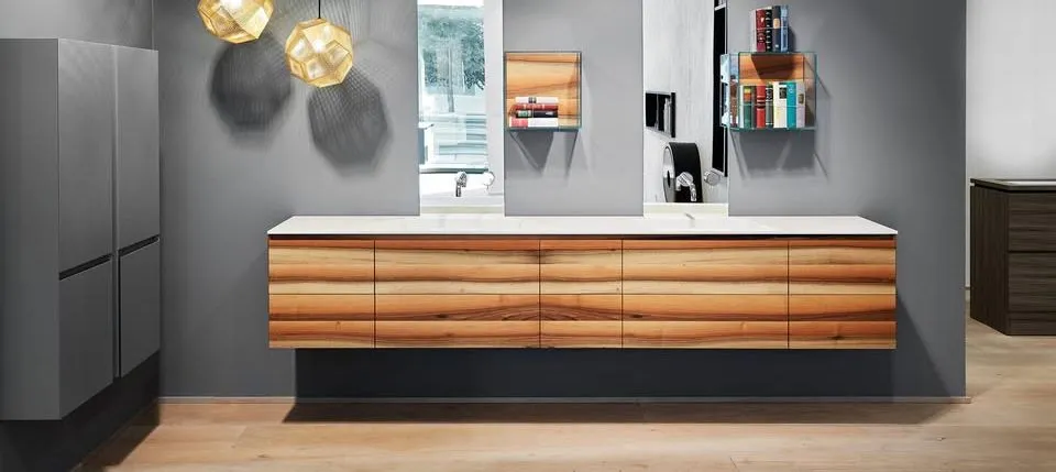 Modernes Badmöbel aus Holz mit weißer Waschtischplatte, großen Spiegeln und goldfarbenen Pendelleuchten.