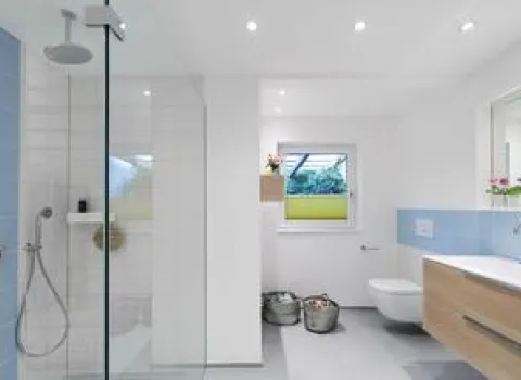 Nordisches Badezimmer mit bodenebener Dusche, blauen Fliesenakzenten, Holzwaschtisch und wandhängender Toilette.