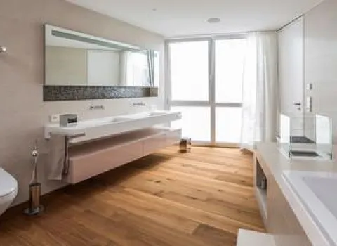 Geräumiges Badezimmer mit Doppelwaschtisch, Holzfußboden, wandhängender Toilette und bodentiefen Fenstern.