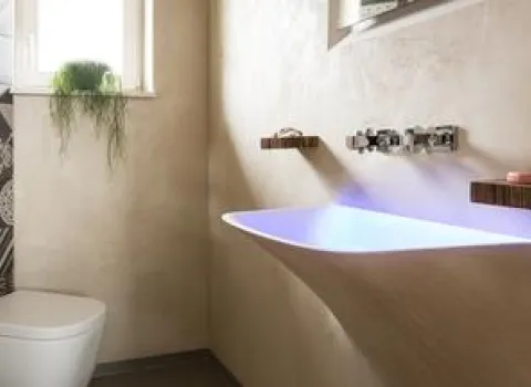 Kleines Gästebad mit beleuchtetem, wandintegriertem Waschbecken, wandhängender Toilette und dekorativen Fliesenakzenten.