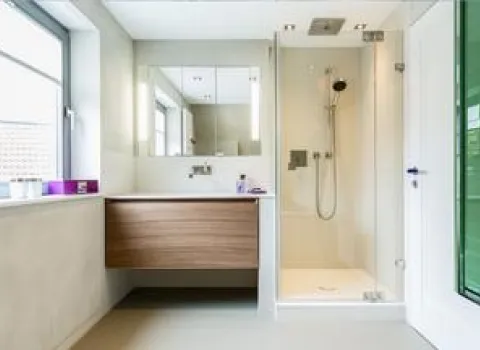 Helles Badezimmer mit bodenebener Glasdusche, modernem Waschtisch mit Holzfront und großem Spiegel.