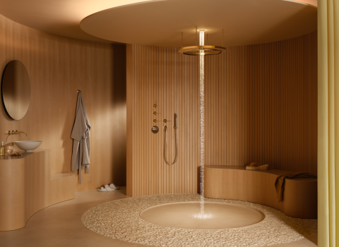 Ein luxuriöses Badezimmer mit einer zentralen, goldenen Regendusche, die einen sanften, schmalen Wasserstrahl in einen runden Kieselsteinbereich fallen lässt. 