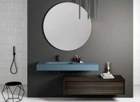 Ausdrucksstarkes Badezimmer von Stocco mit rundem Spiegel, blauem Aufsatzwaschtisch und dunklem Holzunterschrank vor grauer Wand.