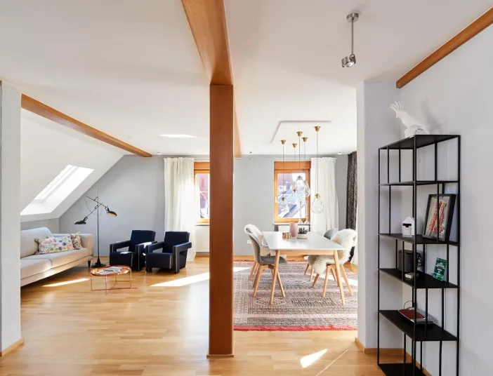 Offenes Wohnzimmer und Essbereich mit Holzboden, modernem Sofa, blauen Sesseln, Esstisch mit Fellstühlen und dekorativem Regal.