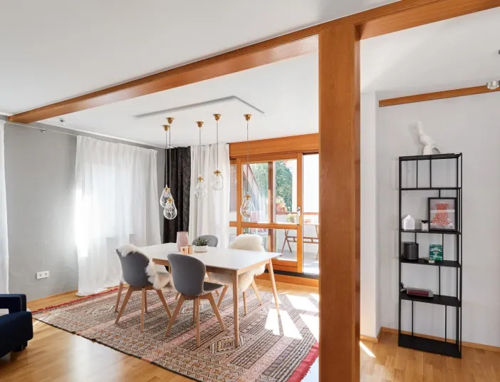 Essbereich mit großem Teppich, weißem Esstisch und Fellstühlen, dekorativen Hängeleuchten und bodentiefen Fenstern mit Blick auf die Terrasse.