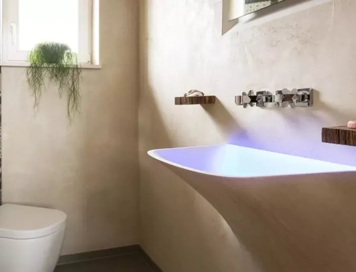 Silberne Armatur über Waschbecken aus matt weißem Mineralwerkstoff mit LED-Beleuchtung